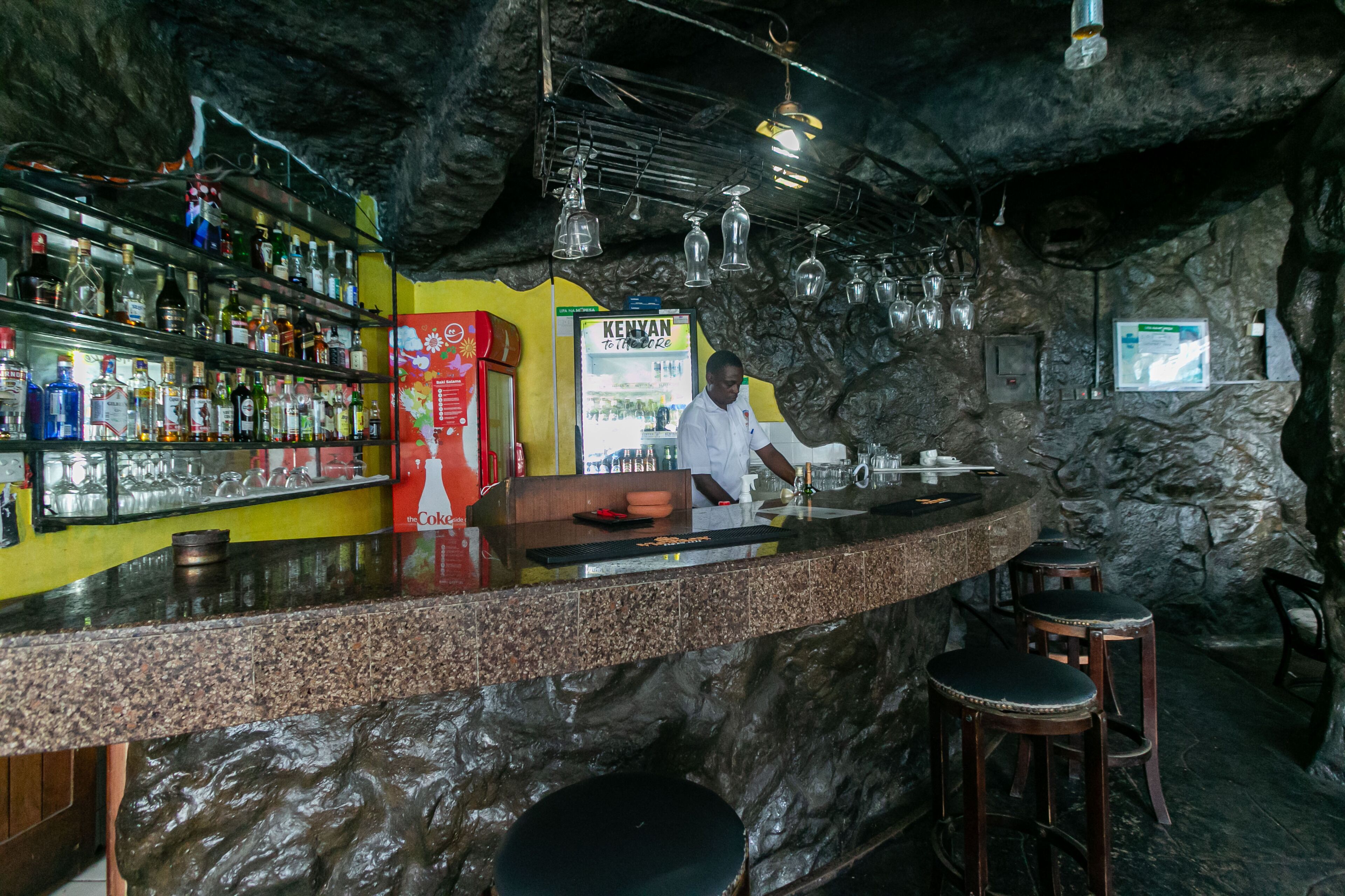 A bar with a granite countertop, shelves of liquor bottles, and a menu board.