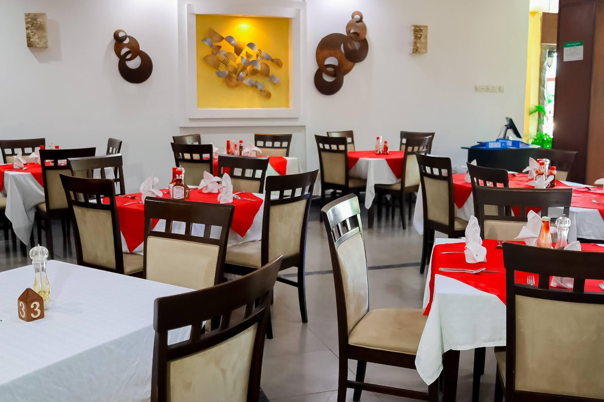 A restaurant with tables covered in red tablecloths, wooden chairs, and a number '33' sign on a table.