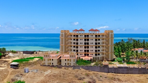 Un hotel de varios pisos con vista a la playa, piscina y estacionamiento.