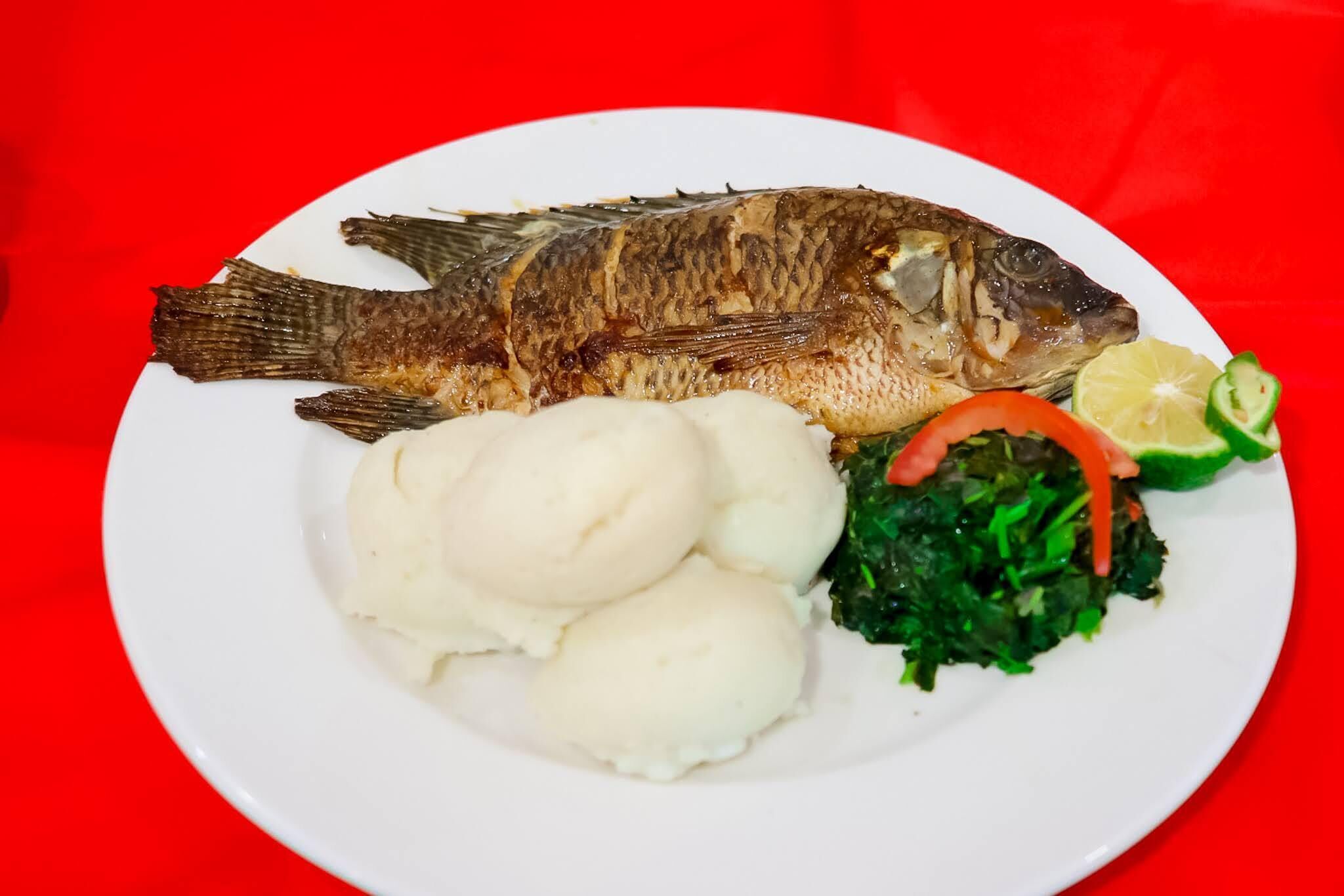 A plate with a whole fish, mashed potatoes, and greens.