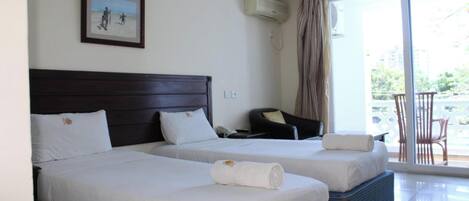 A hotel room with two beds, a chair, a small table, and a balcony with chairs.