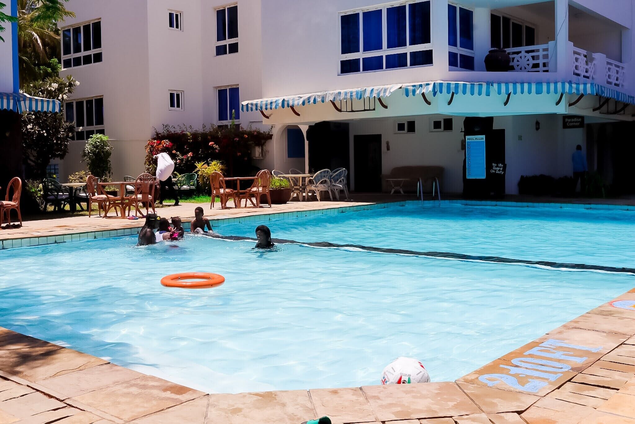 A swimming pool with lounge chairs and tables, a building with a balcony, and a sign indicating a room for sale.