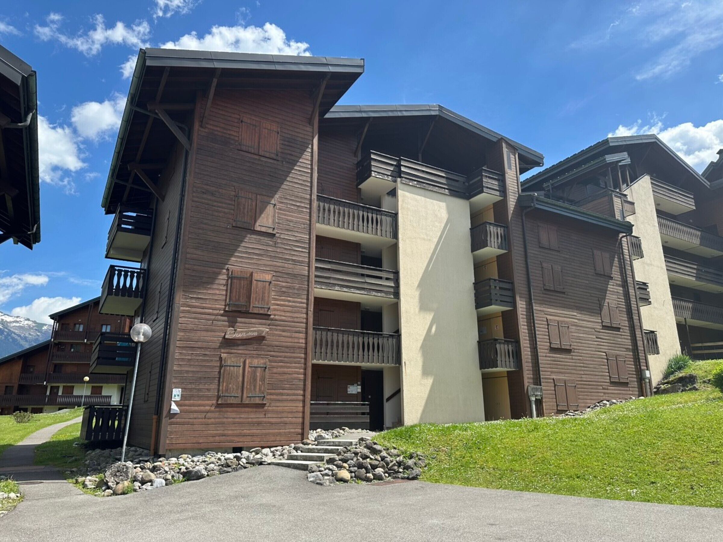 Un immeuble à plusieurs étages, doté d’une façade en bois, de balcons et d’un chemin en pierre menant à l’entrée.