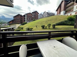A terrace with a view of a hillside, wooden buildings, and a mountain in the background.