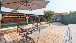 Een houten terras met een zwembad, zitplaatsen buiten en een overdekt gedeelte met een bord.