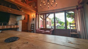 Een rustiek interieur met een houten tafel, rieten manden, een kroonluchter en grote ramen met uitzicht.