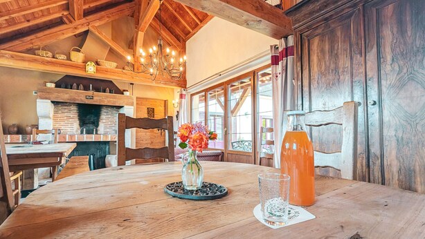 Een houten eettafel met een bloevas, een glas sinaasappelsap en een waterfles.