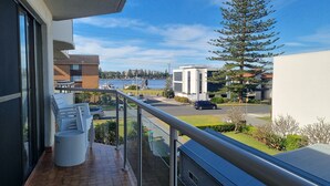 A balcony with a view of a waterfront, a parking area, and modern buildings. - Welcome to Champagne Court 07 (Tuncurry)
