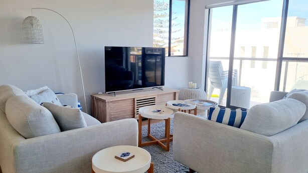 A modern living room with a flat-screen TV, two sofas, a coffee table, and a side table. - Welcome to Champagne Court 07 (Tuncurry)