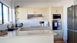 A modern kitchen with a large island, stainless steel appliances, and light-colored cabinetry. - Welcome to Champagne Court 07 (Tuncurry)