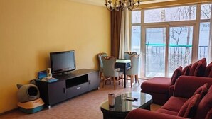 A living room with a TV, a sofa, a coffee table, and a dining area with chairs. - RGHCM Garden Resorts (Beijing)