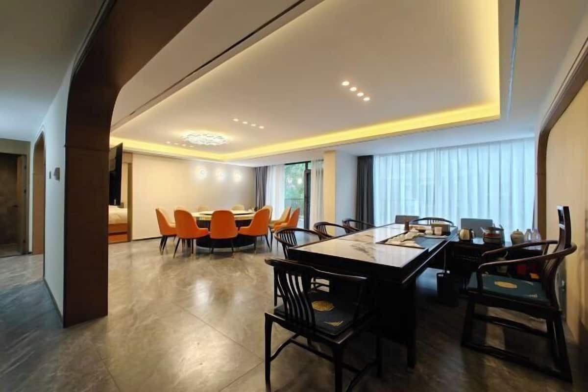 A modern dining area with a marble table and chairs, a separate seating area with orange chairs, and a large window with curtains.