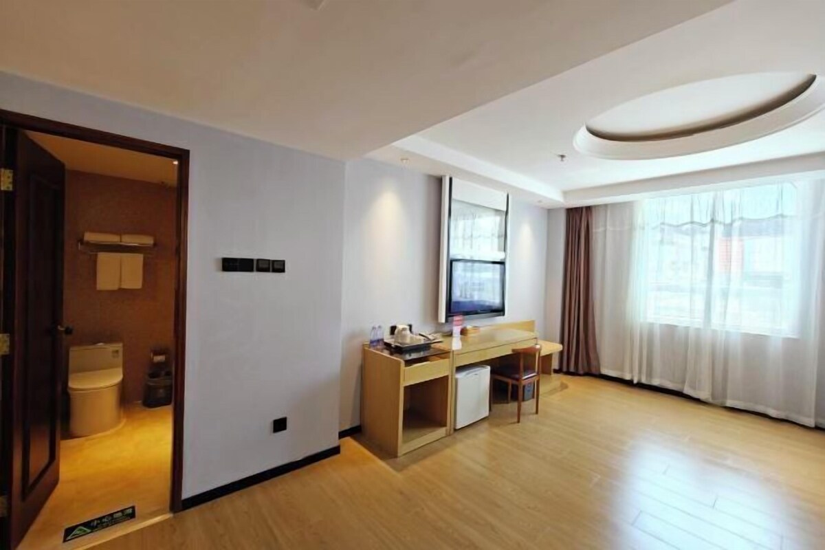 A modern hotel room with a wooden floor, a desk with a chair, a television, and a large window with curtains.
