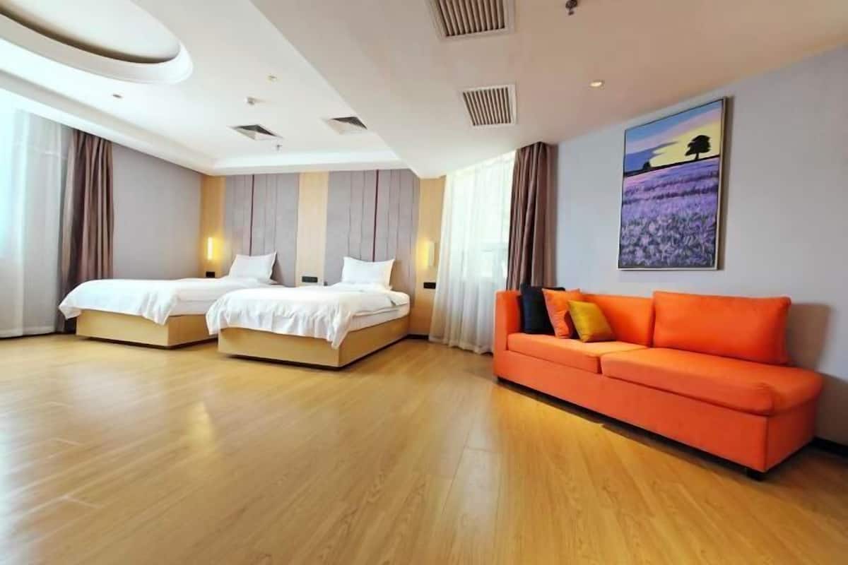 A hotel room with two beds, an orange sofa, and a painting on the wall.