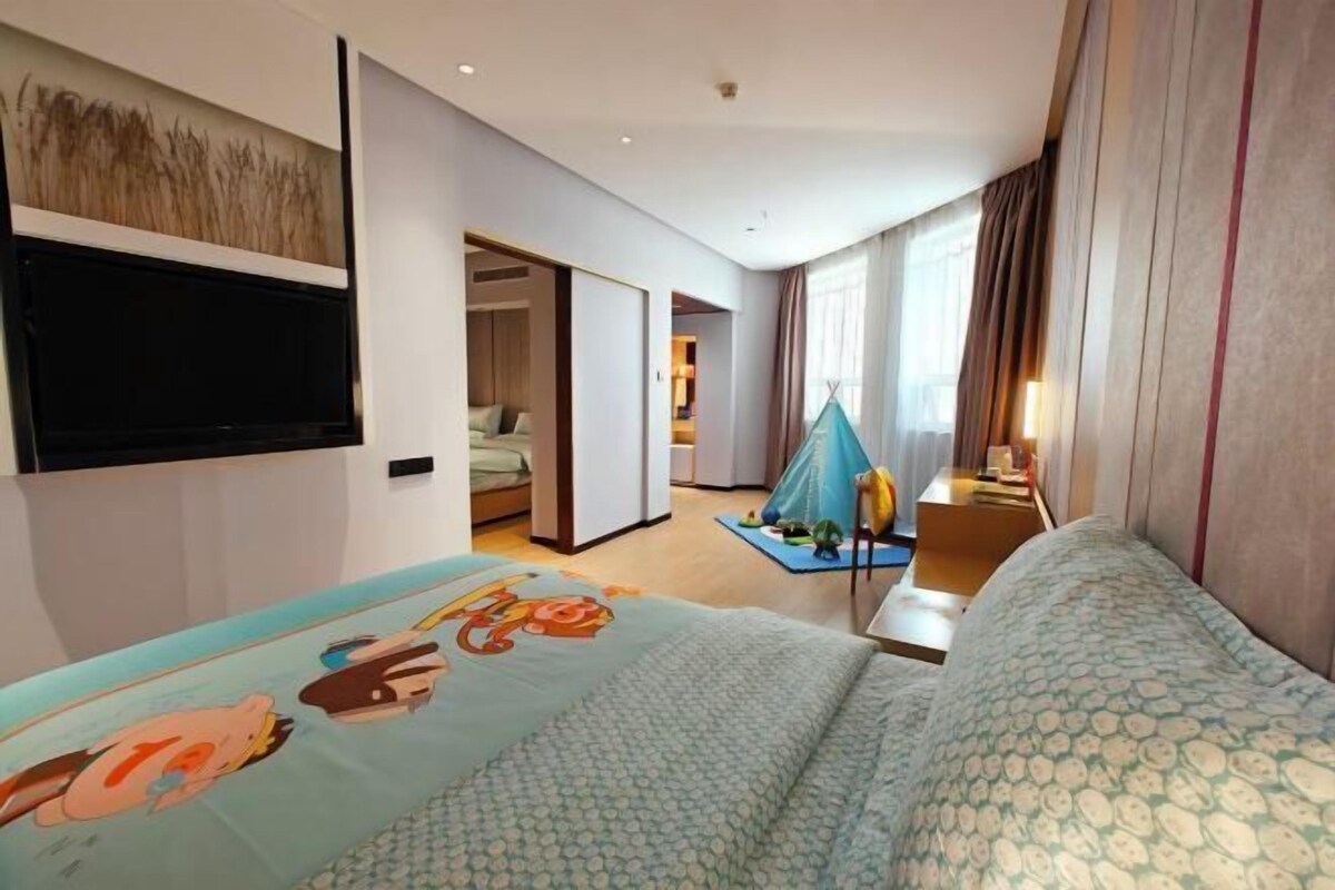 A hotel room with a bed, a flat-screen TV, a desk, and a window with curtains.