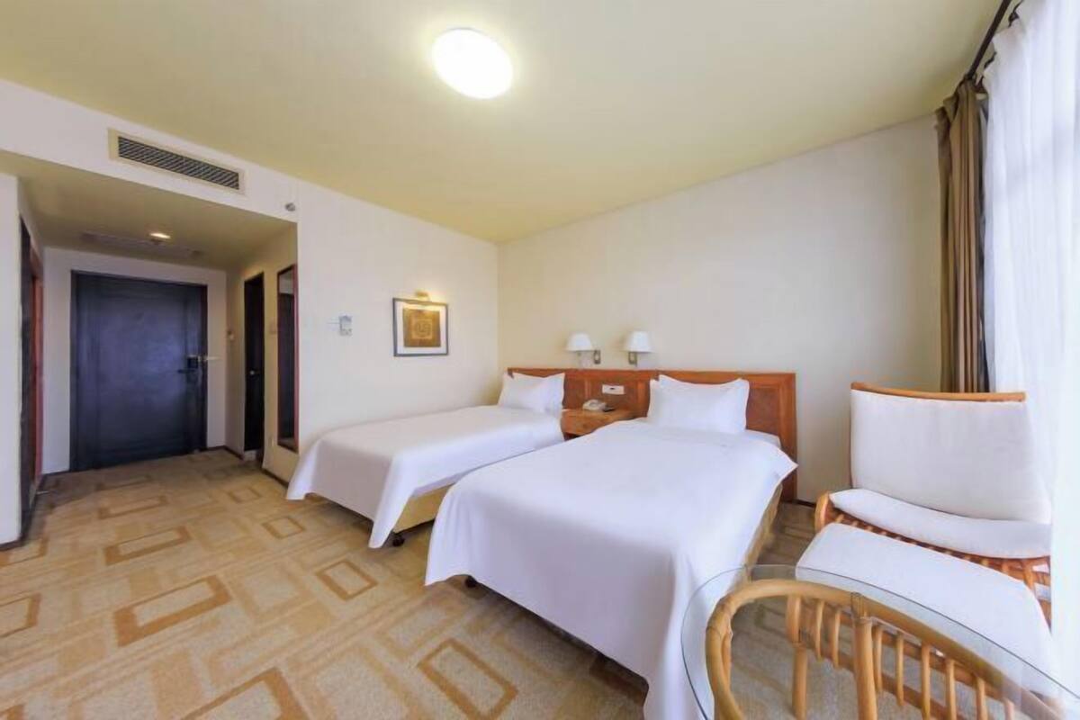 A hotel room with two beds, a wooden headboard, a chair, and a door.