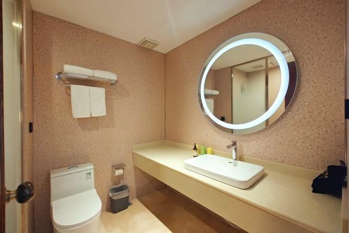 A bathroom with a round mirror, a white sink, a towel rack, and a toilet.