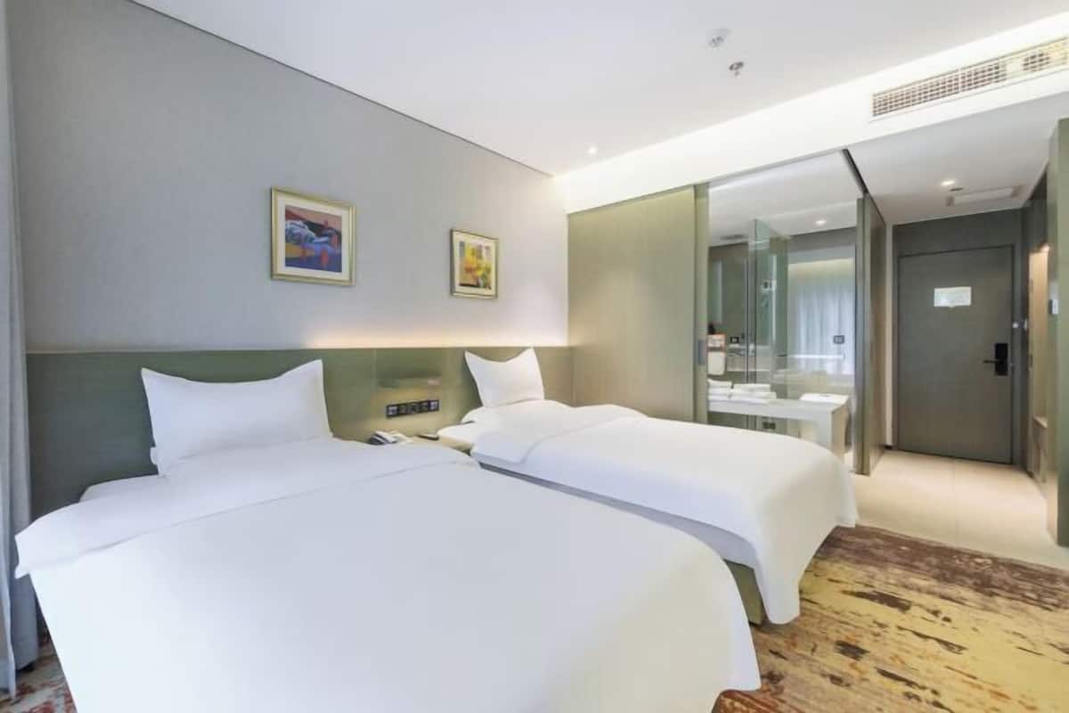 A hotel room with two beds, a large mirror, and a bathroom visible through a glass door.