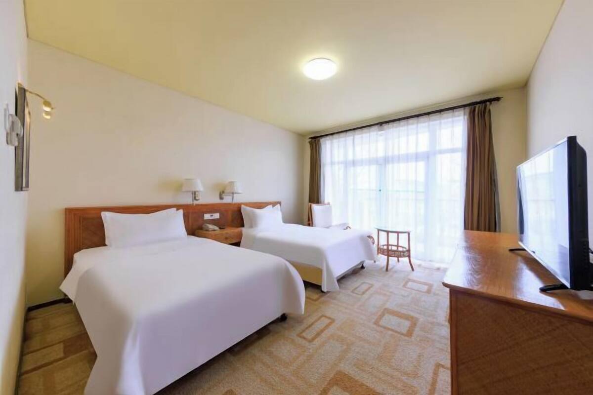 A hotel room with two beds, a desk, a television, and a window with curtains.