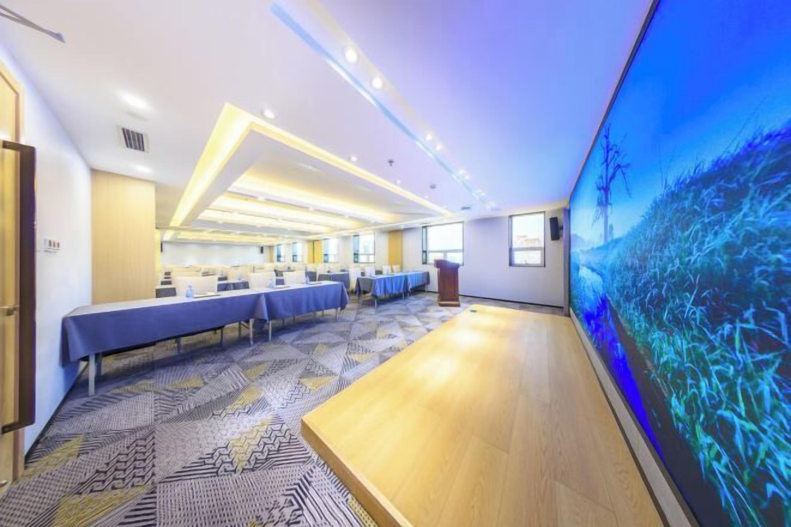 A conference room with a long table, multiple chairs, and a large digital screen displaying a nature scene.