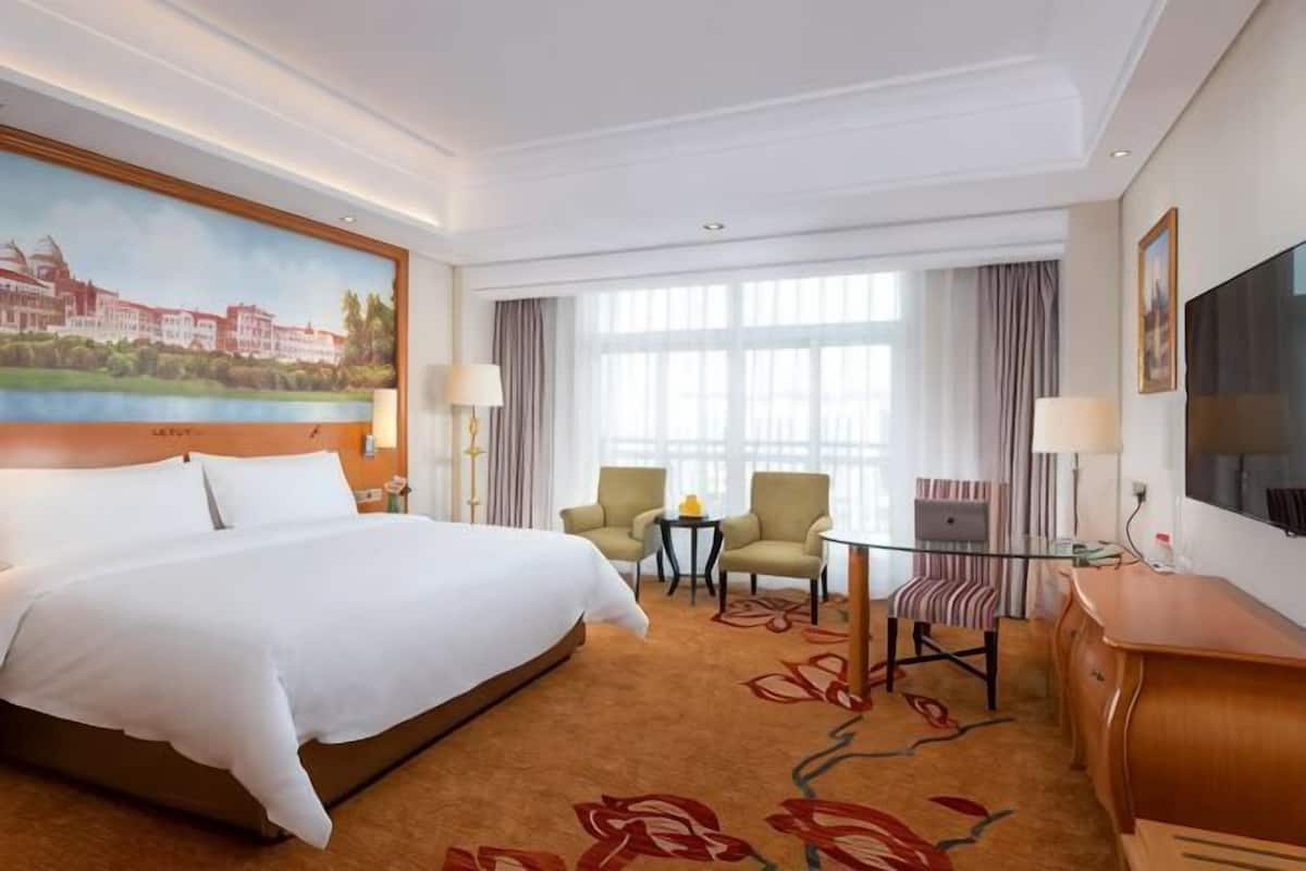 A hotel room with a large bed, a desk with a chair, a small table, and a TV.