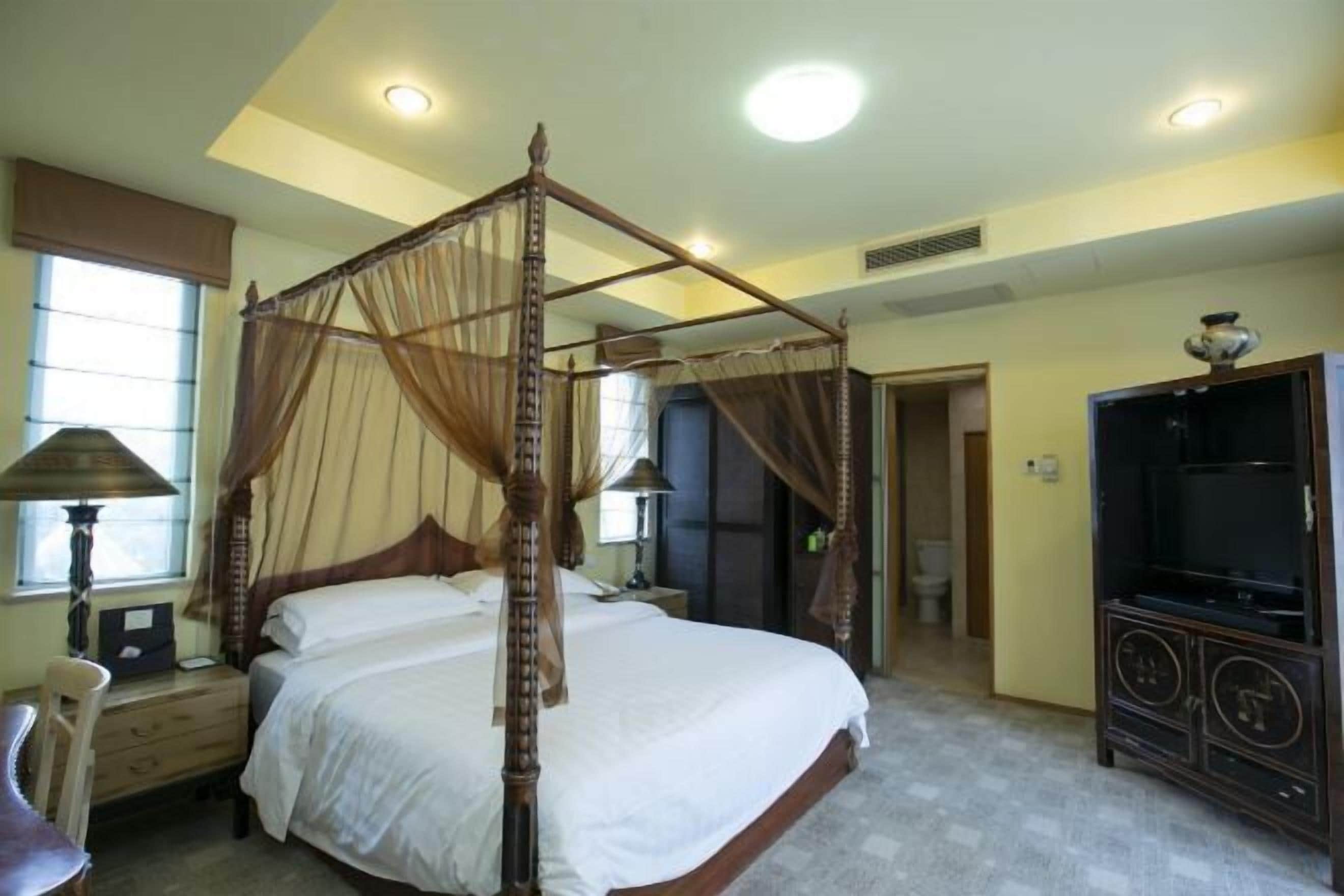 A four-poster bed with a canopy, a television, a desk, and a chair in a hotel room.