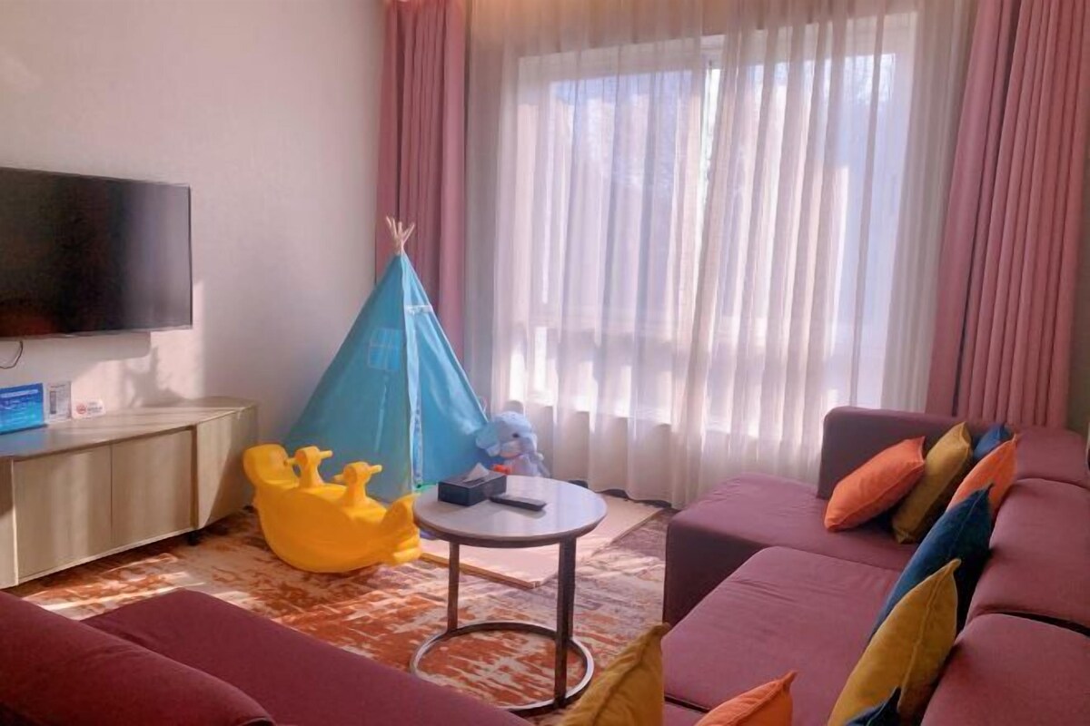 A living room with a flat-screen TV, a sofa, a small round table, and a colorful play tent.