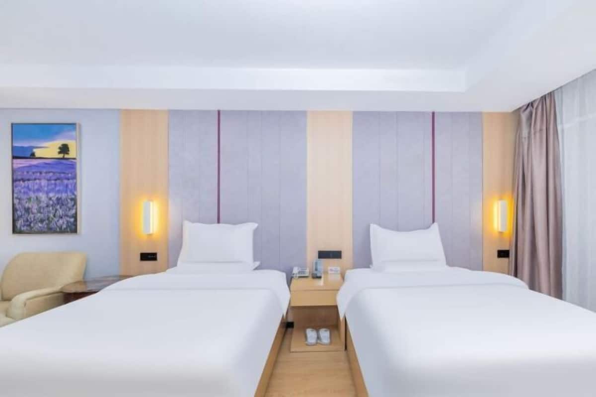 A hotel room with two beds, a chair, a painting on the wall, and a nightstand with a phone.