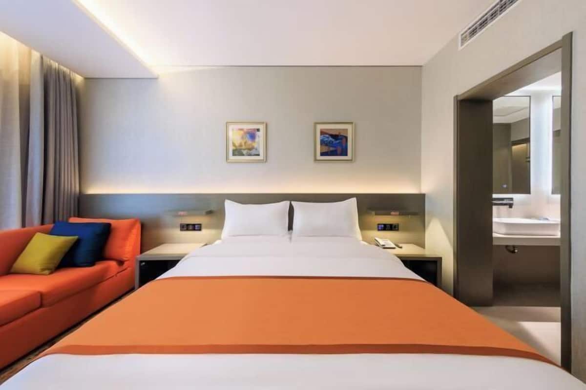 A hotel room with a bed, a nightstand, a red sofa, and two framed pictures on the wall.