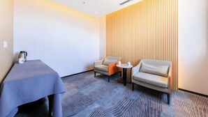 A hotel room with a grey carpet, a table with a kettle, two armchairs, and a small round table with a cup. - RGHCM Garden Resorts (Beijing)