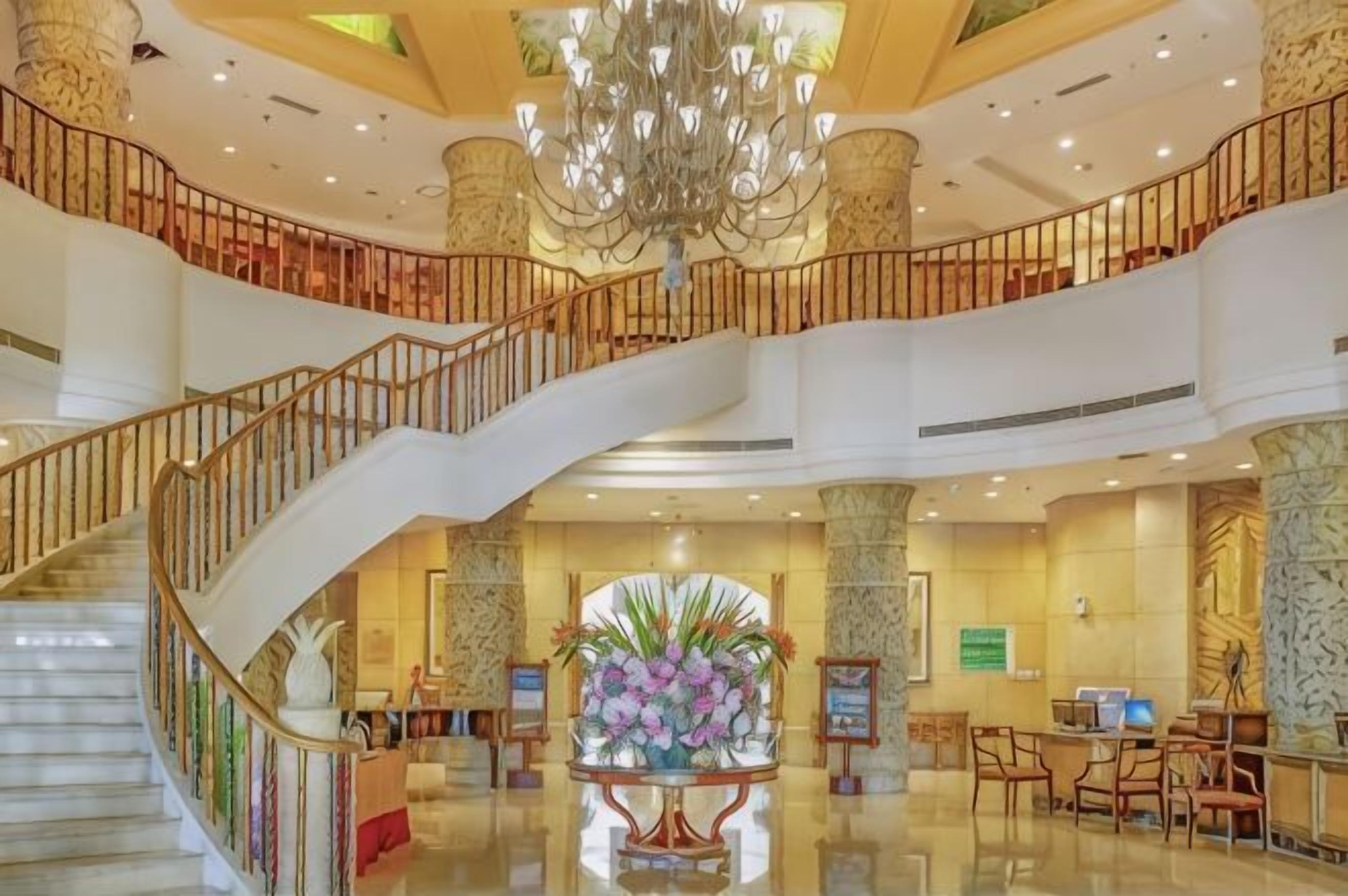 A grand lobby with a marble staircase, a chandelier, and a reception desk.