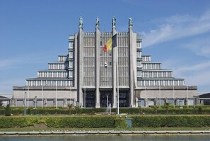 Um edifício grande e simétrico, com entrada central e várias estátuas no telhado.