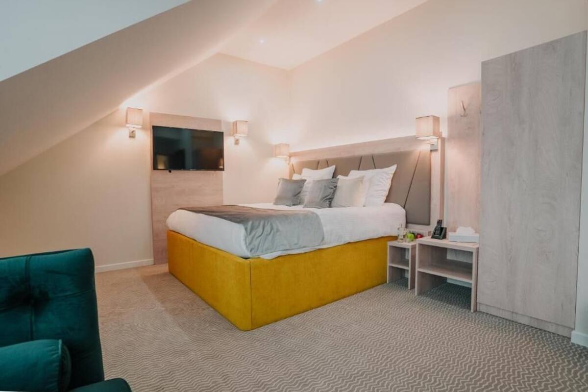 A modern bedroom with a yellow bed, two bedside tables, a TV mounted on the wall, and a large wardrobe.