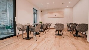 Un comedor moderno con varias mesas y sillas, ventanas grandes y una escalera visible a través del muro de cristal.