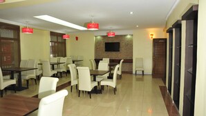 A dining area with tables and chairs, a flat-screen TV mounted on the wall, and a wooden door labeled "Restaurant". - Nomad Paradise Hotel (Nairobi)