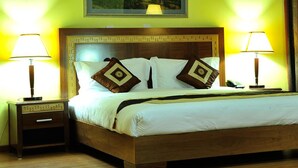 A neatly made bed with a wooden headboard, two bedside lamps, and a small drawer unit. - Nomad Paradise Hotel (Nairobi)