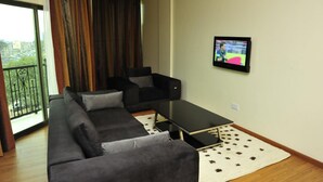 A modern living room with a sectional sofa, a small black table, and a TV mounted on the wall. - Nomad Paradise Hotel (Nairobi)