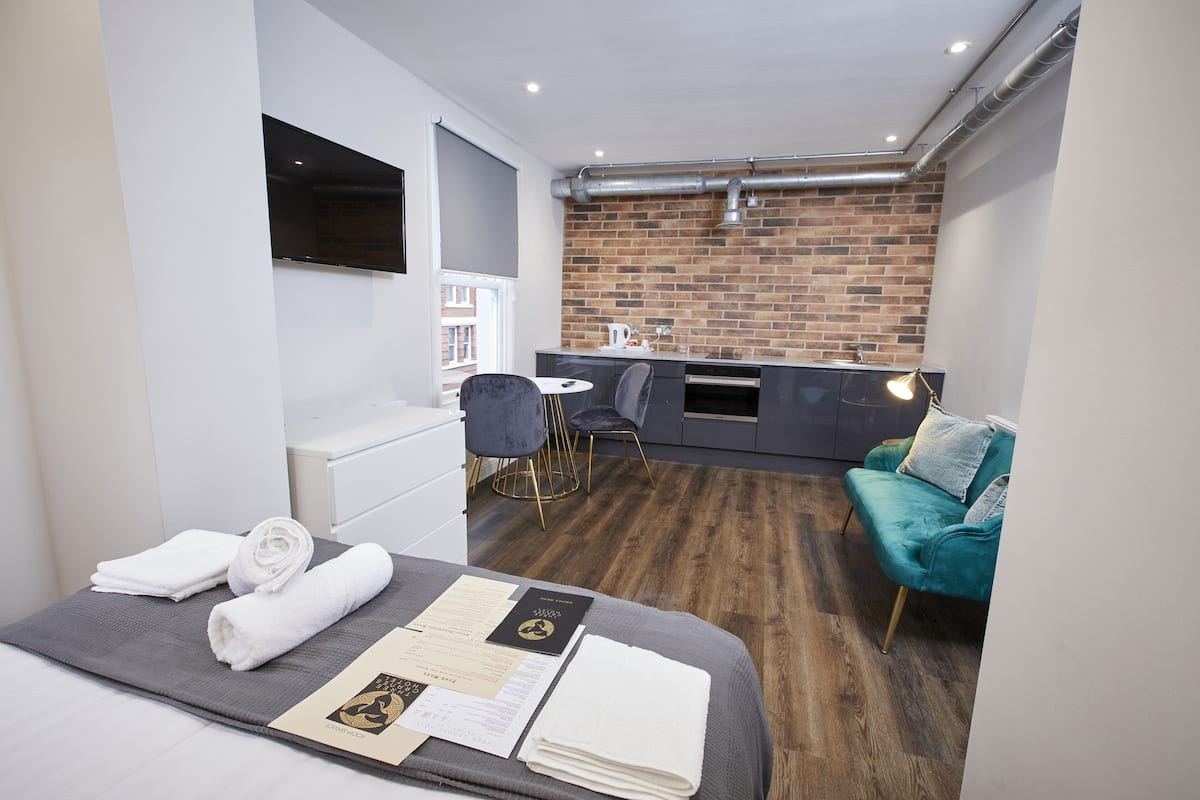 A modern hotel room with a bed, a dining area, and a kitchen.