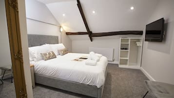 A modern bedroom with a large bed, a built-in TV, and a cozy reading nook.