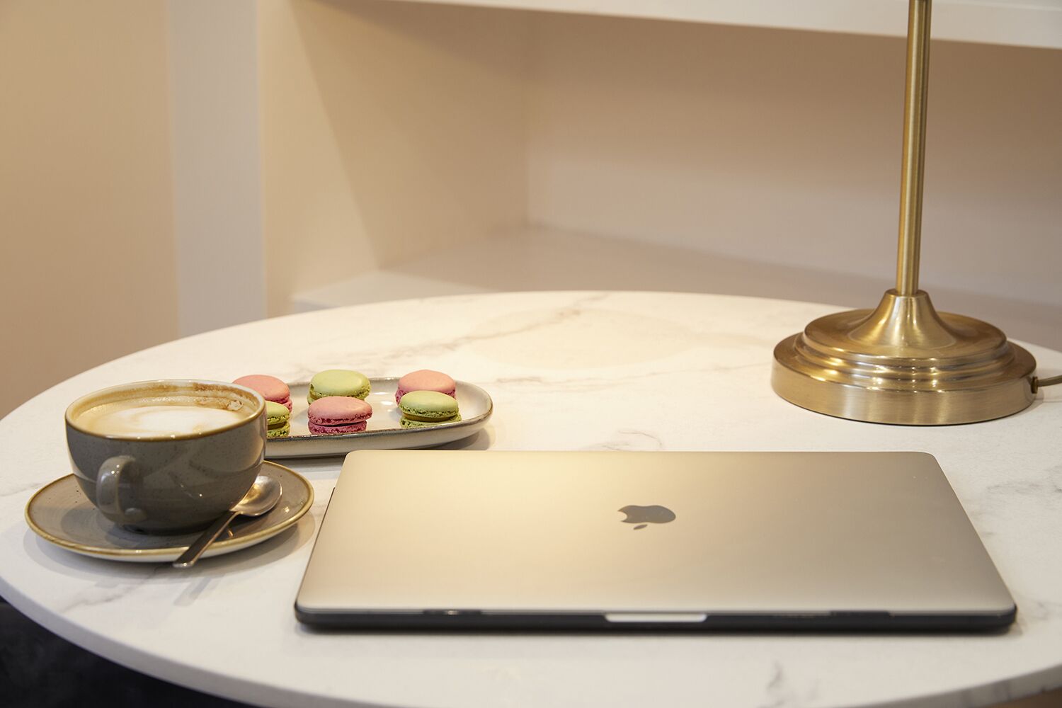 A laptop, a cup of coffee, and a plate of macarons on a marble table.