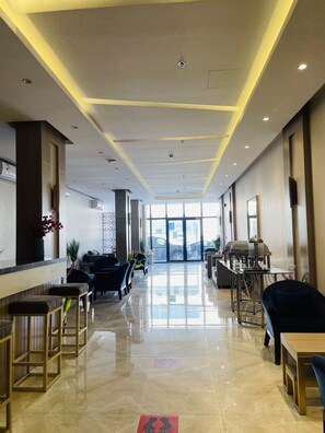 A hotel lobby with a long reception desk, seating area, and a view of the outside.