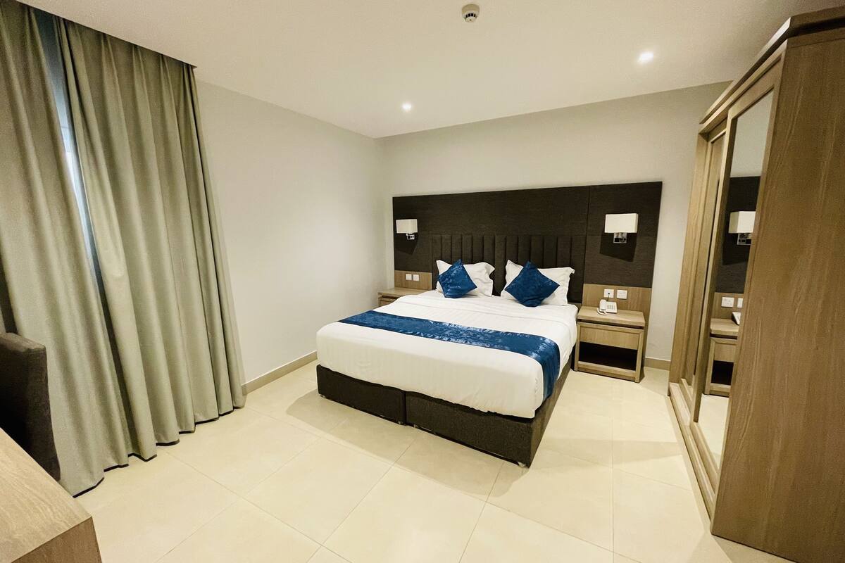 A modern hotel room with a large bed, bedside tables, a mirror, and a view of the outside.