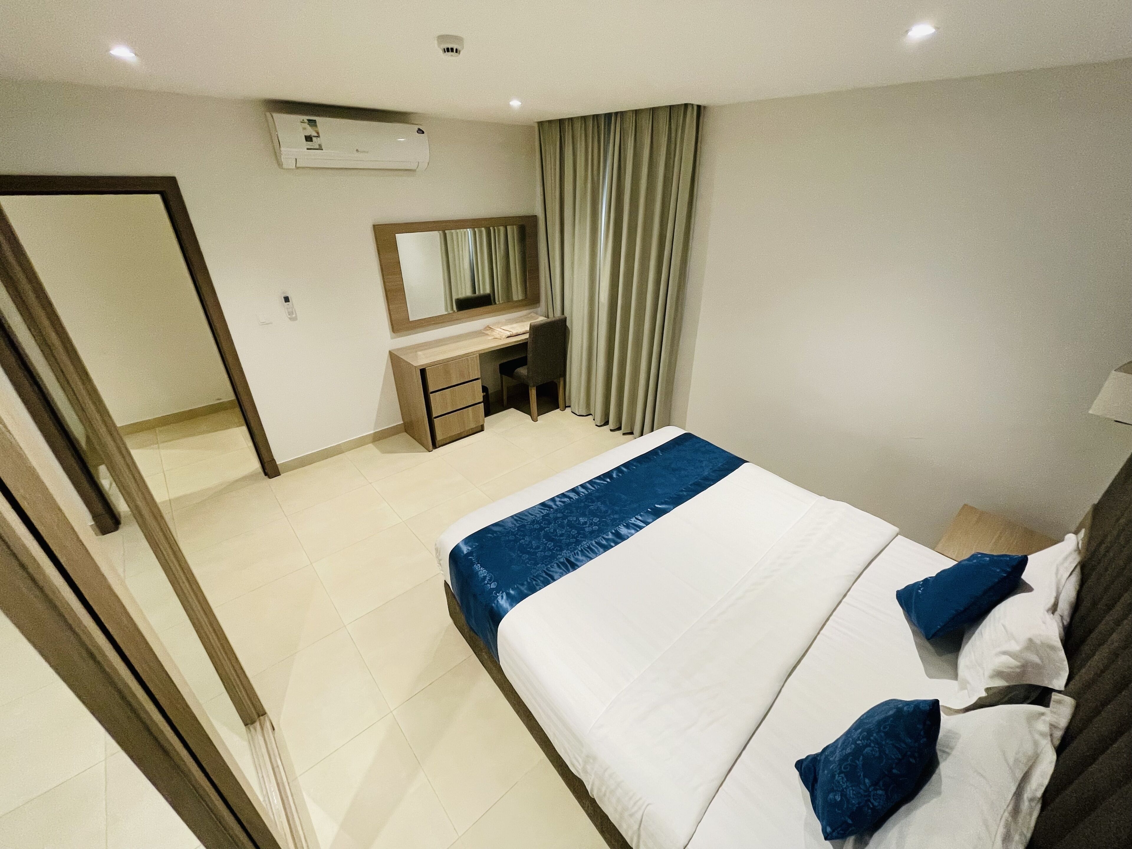 A hotel room with a bed, a desk, a chair, a mirror, and a window with curtains.