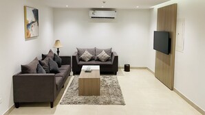 Ein modernes Wohnzimmer mit zwei Sofas, einem Couchtisch, einer Lampe, einer Klimaanlage und einem an der Wand befestigten Fernseher.