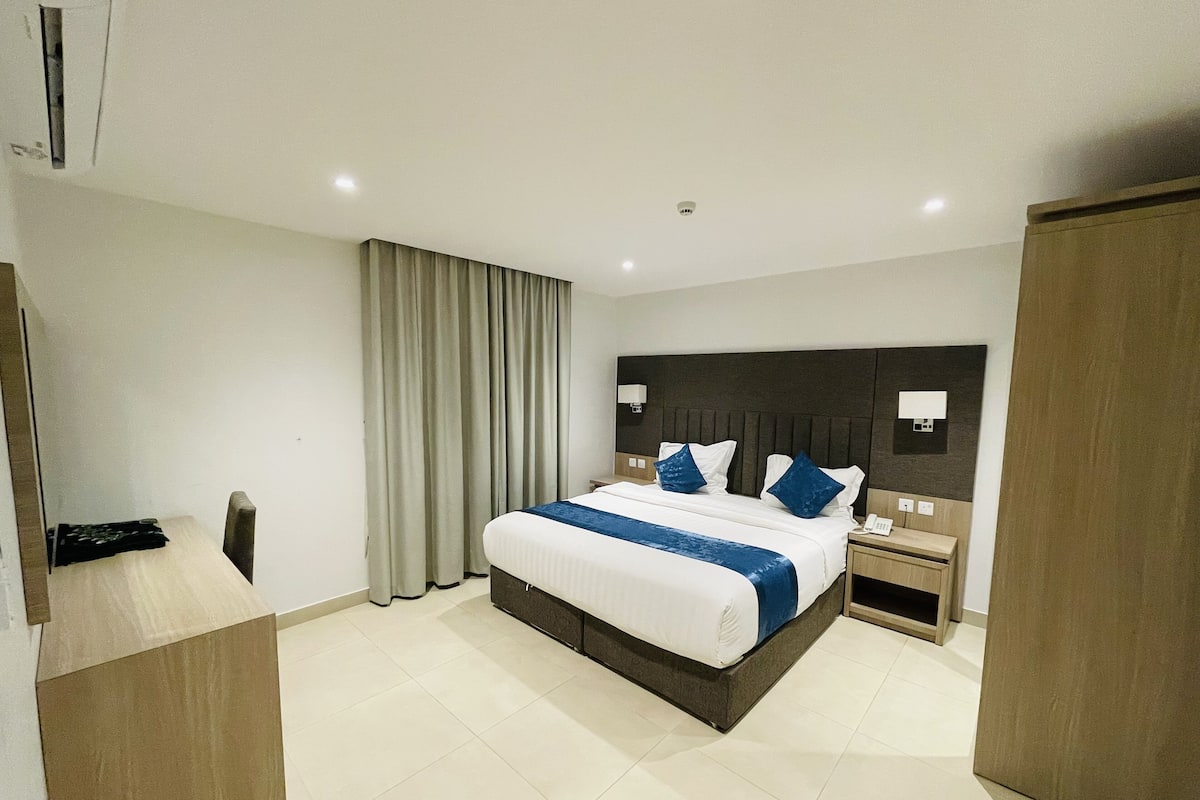 A hotel room with a large bed, a bedside table, a nightstand, a wardrobe, and a curtain.