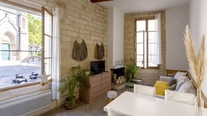 A cozy living room with a stone wall, a television, a fireplace, and a view of a street with outdoor seating. - L'Esprit Montpel "Face à l'Eglise St Roch" (Montpellier Spirit) (Montpellier)