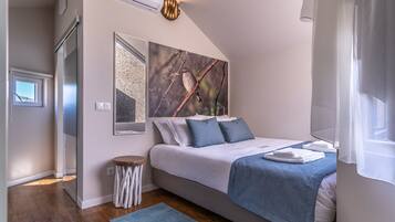 A bedroom with a bed, a mirror, a wall-mounted air conditioner, a small stool, and a window with a view.