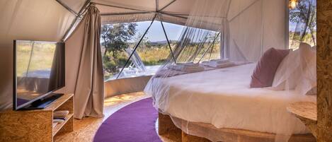 A tented room with a bed, a television, and a view of the outdoors.