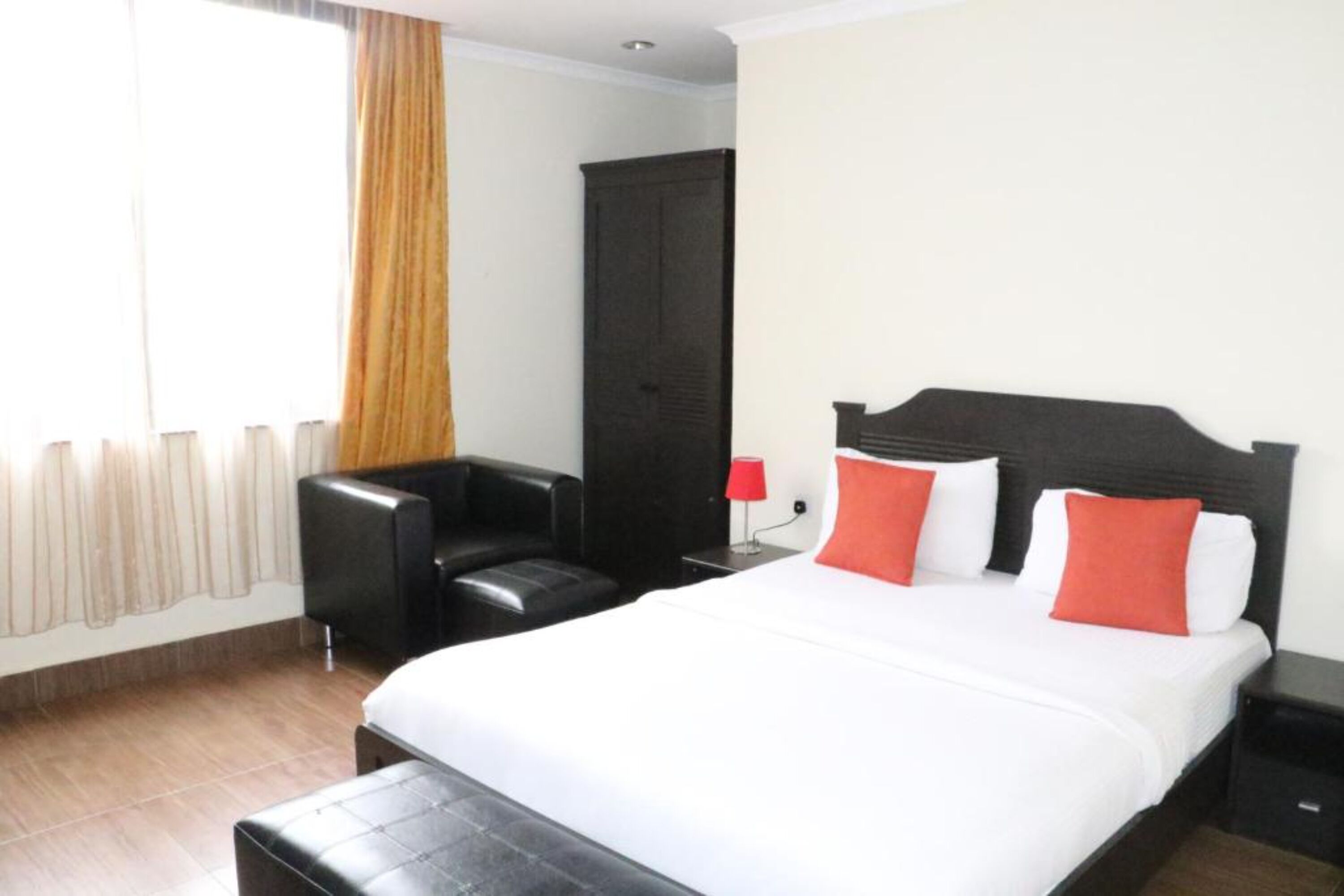 A hotel room with a bed, a chair, a wardrobe, and a nightstand.