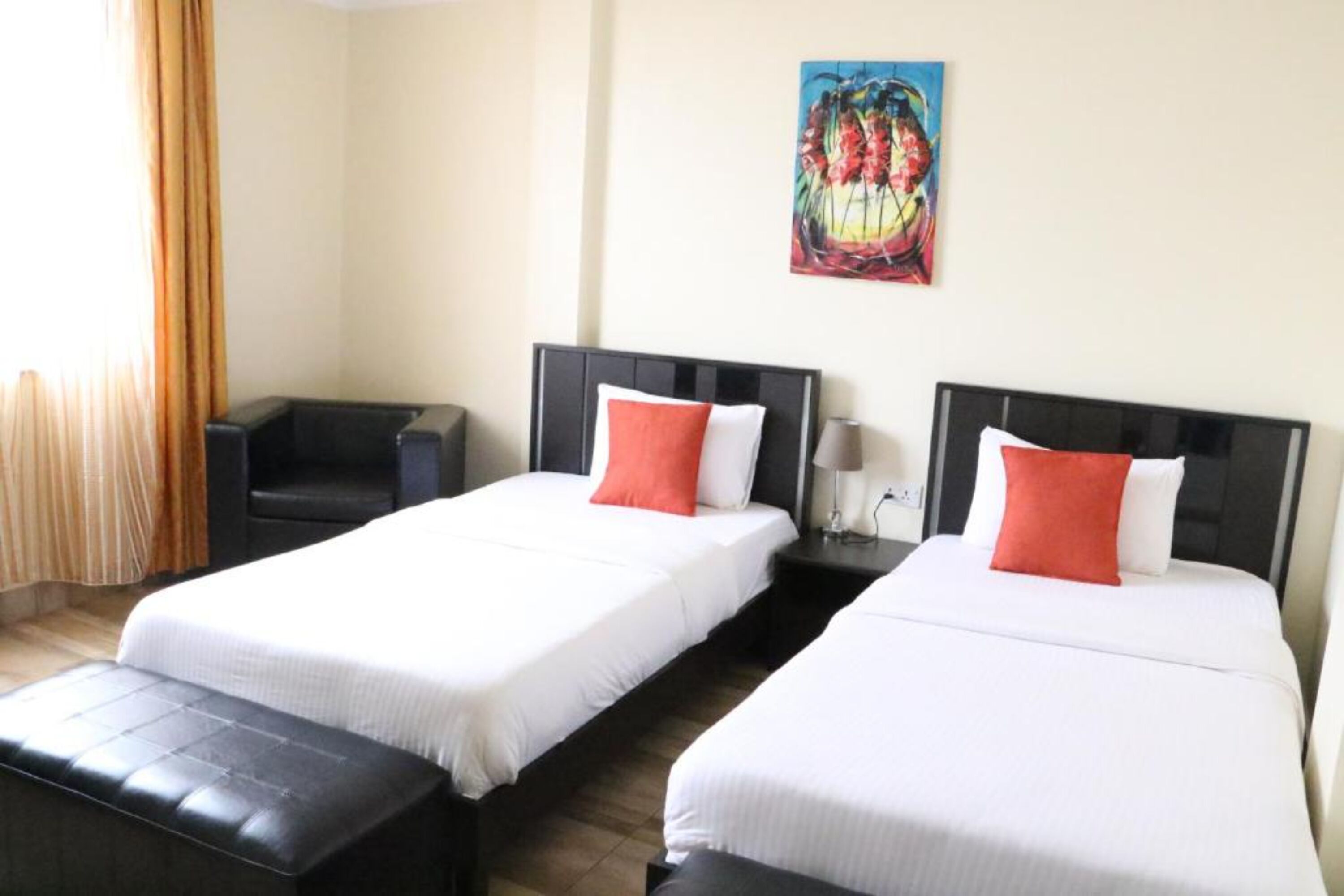 A hotel room with two single beds, a black leather sofa, a painting on the wall, and a window with curtains.